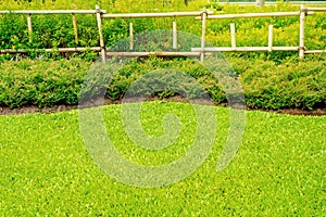 Flowerbeds with green grass in the garden, fence made of bamboo, Garden with a Freshly Mowed Lawn.