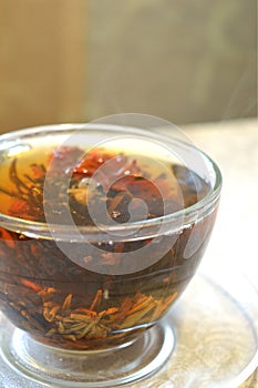 Flowering tea in the transparent cup on transparent saucer, the steam from the hot tea