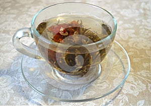 Flowering tea in the transparent cup on transparent saucer and on tablecloth with white roses