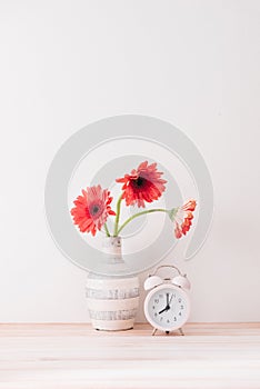 Flowers and alarm clock on a white wall shelf