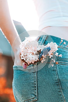 Flowers in the back pocket of blue jeans, a girl with red manicure
