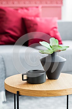 Flowers in black vase next to black coffee cup on wooden coffee table in stylish interior