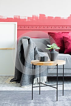 Flowers in black vase next to black coffee cup on wooden coffee table in stylish interior