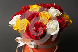 Flowers in bloom: A bouquet of red and yellow roses in a round box on a grey background.