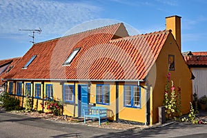 Flowers blossoming in front of the traditional half-timbered yellow house in the town of Gudhjem