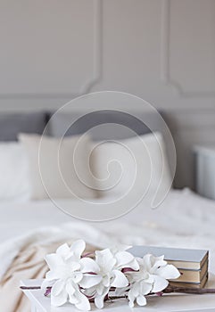 Flowers and books in front of comfortable bed in classy bedroom interior