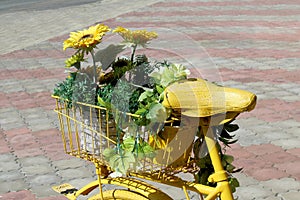 A yellow decorative bicycle with flowers stands in the parking lot on a summer day.