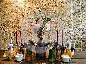 Flowers bouquet in vase on wooden stylish table, candles, brick wall on background. Wooden furniture stylish background