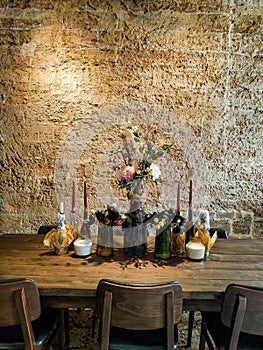 Flowers bouquet in vase on wooden stylish table, candles, brick wall on background. Wooden furniture stylish background