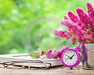 Flowers in bucket, pink alarm clock and book
