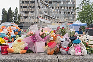 Flowers and children toys at the place where the children died. In the background, a civilian building was damaged by an