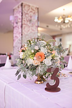 Flowers composition with orange and beige flowers and number three on the table for guests on wedding hall. Wedding table number.