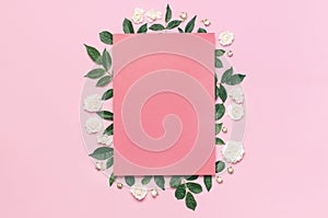 Flowers composition. Pink blank paper, white fresh roses and green leaves on gentle pink background. Flat lay, top view, copy
