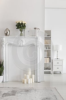Flowers on elegant portal above candles in white apartment interior with grey carpet. Real photo