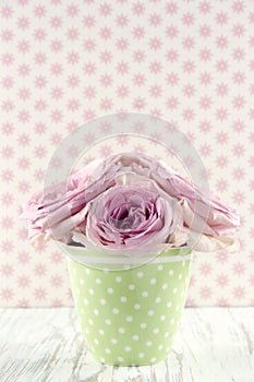 Flowers in a green polkadot vase on vintage wooden background