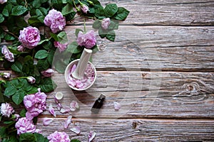 Flowers and leaves of rosehip,  petals in a mortar with a pestle and a bottle of essential oil on a wooden background.