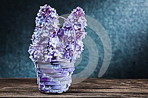 Flowers of lilac in little wicker basket on vintage wood and black background