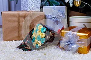 flowers made of chocolate under Christmas tree with white branches among beautiful gift boxes.