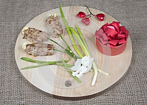 Flowers made of meat on wooden cutting board, red hearts and natural burlap background. Food art idea for Valentine day, birthday