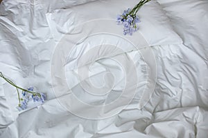 Flowers on the messy bed, white bedding items and blue flowers bouqet