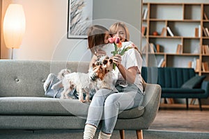 With flowers. Mother with her daughter and with two cute dogs is in domestic room