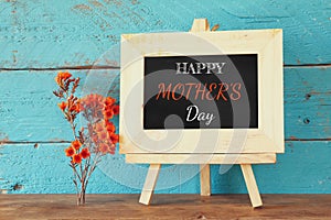 Flowers next to blackboard with phrase: HAPPY MOTHERS DAY, on wooden table. happy mother's day concept