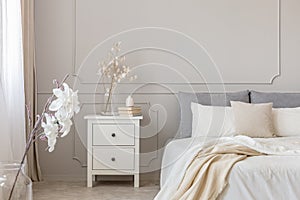 Flowers on nightstand table in delightful bedroom interior with grey and white design