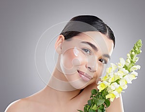 Flowers pale in comparison. Studio portrait of an attractive young woman posing with a bunch of flowers against a grey