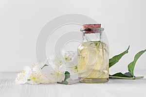 Flowers of philadelphus somewhere called jasmine or mock orange and a bottle of oil on a white wooden table