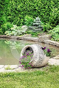 Flowers are planted in broken decorative pot near the pond