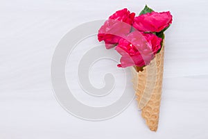 Flowers red roses in a waffle cone on white wooden background. Flat lay, top view, floral background