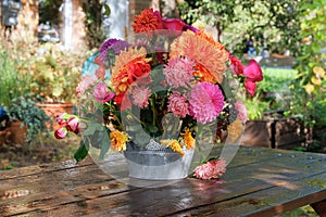Flowers: roses, asters, dahila in the apple garden on a wooden table. Floristic design. Sunny day
