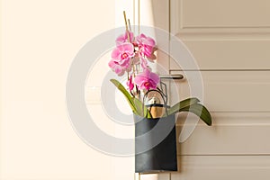 Flowers surprise on the door handle. Pink orchid in gift bag on white door in the room