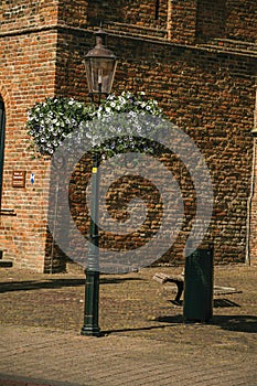 Flowers on top of public lamp post in front of church facade made of bricks in a sunny day at Weesp.