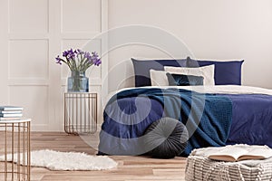 Flowers in vase on bedside table next to king size bed with navy blue bedding