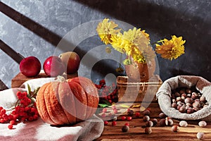 Flowers in a vase and fresh whole vegetables: pumpkin, apples, corn and hazelnuts in a bag