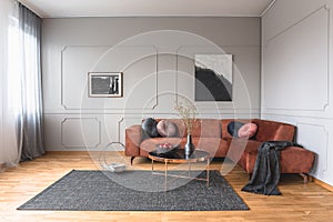 Flowers in vase and red fruits in bowl on wooden coffee table in elegant living room with ginger sofa