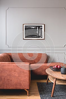 Flowers in vase and red fruits in bowl on wooden coffee table in elegant living room interior with ginger sofa