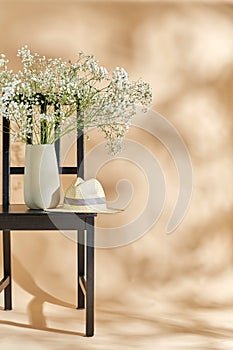 flowers in vase and straw hat on chair over beige