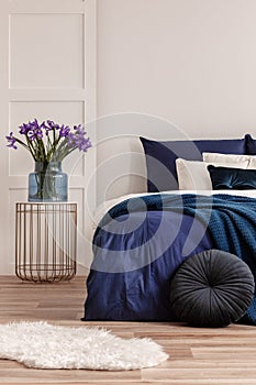 Flowers in vase on stylish nightstand in bright bedroom interior