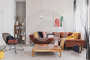 Flowers in vase on wooden coffee table in fashionable living room interior with brown corner sofa with pillows and abstract