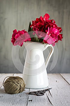 Flowers in white enamel pitcher on a white wooden surface