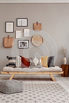 Flowers in white vase on small wooden table behind comfortable futon sofa with pillows