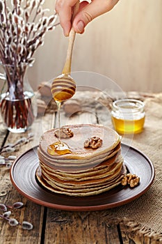 Flowing honey on stack of pancakes with nuts