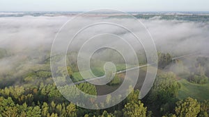 Flowing mist above early morning landscape with forest and road, aerial