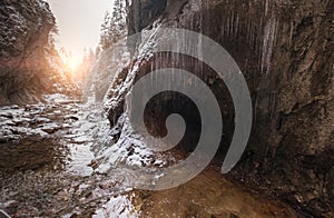 Flowing small creek running out icicle cave and washing big boulders. First sun rays lite young snow islands. Cold early winter