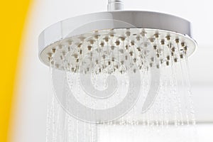 Flowing water drops from a shower head in a white bright bathroom