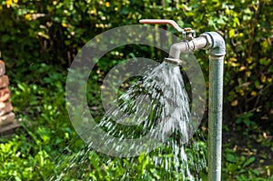 Flowing water on the garden tap , green blurry background,