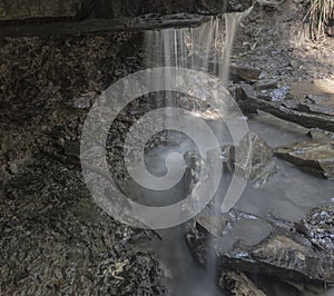 A flowing waterfall from behind a rock ledge into a pool of water photo