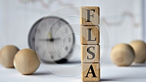 FLSA - acronym on wooden cubes on graph, clock and wooden balls background